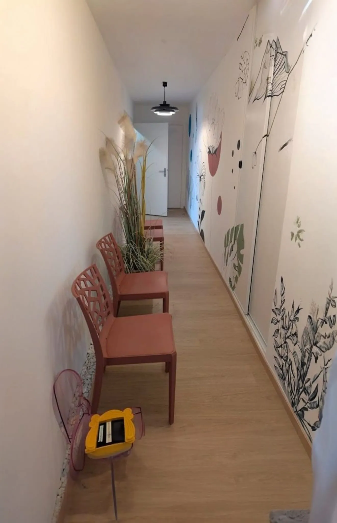L’espace d’attente : quelques chaises le long d’un couloir orné d’une fresque végétale.
